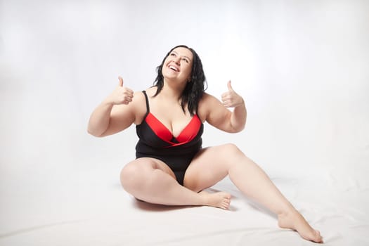 Portrait of attractive dreamy thick woman in red black swimsuit posing on white background. Body positive, photoshoot, selfie. Funny plus size model