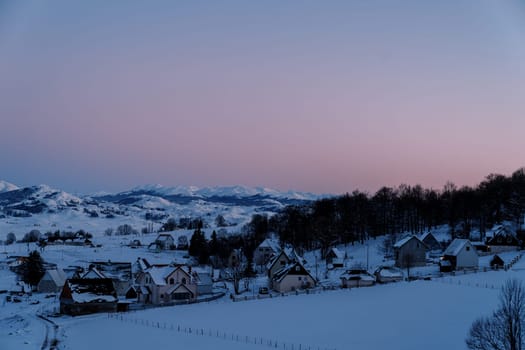 Pink sunset over a snow-covered small village in a mountain valley at the edge of the forest. High quality photo