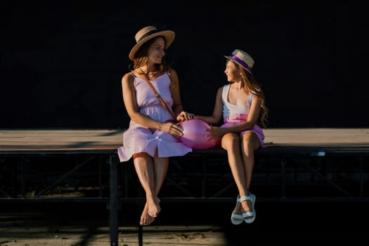 mother and daughter are sitting in pink dresses with flowing long hair on a black background. Enjoy communicating with each other.