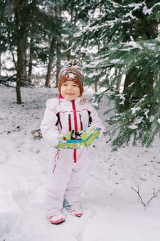 Little smiling girl stands near a snow-covered fir tree. High quality photo