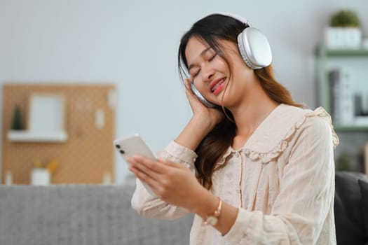 Pleasant young woman listening to music in headphones with closed eyes, relaxing and dreaming