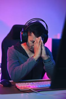 Shot of male gamer in headphones looking upset while playing a game losing to an opponent