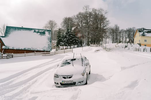 Snow-covered car stands in a snowdrift in a small village. High quality photo
