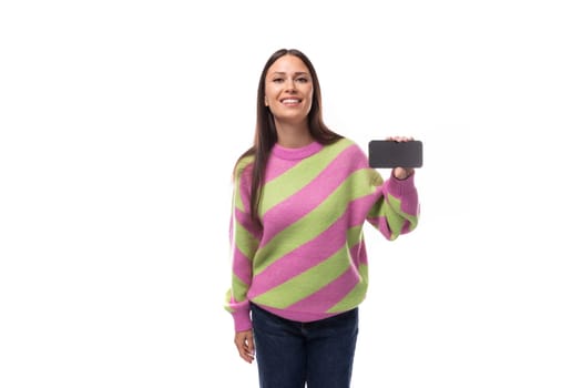 young slender caucasian woman with straight black hair dressed in a striped pink pullover holds a phone horizontally screen forward with a mockup for advertising.