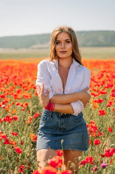 Happy woman in a poppy field in a white shirt and denim skirt with a wreath of poppies on her head posing and enjoying the poppy field