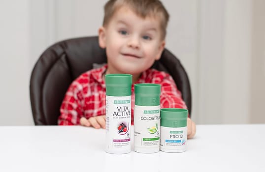 Dnepr, Ukraine - January 03,2024: a small handsome boy is sitting at a table with products from the cosmetic company LR Health and Beauty, vitamins, probiotic, colostrum. Close-up