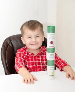 Dnepr, Ukraine - January 03,2024: a small handsome boy is sitting at a table with products from the cosmetic company LR Health and Beauty, vitamins, probiotic, colostrum. Close-up