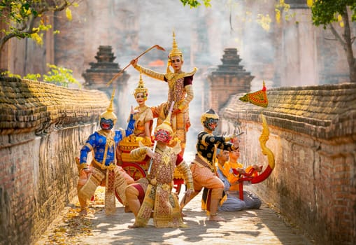 Group of Khon or traditional Thai classic masked from the Ramakien characters stand together with action of traditional dance with Thai ancient building in background of public place.