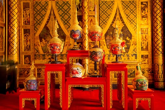 Beautiful ancient traditional Thai pattern Pantomime or Khon masks are set up on wooden shelves with Thai painting as background of public place in Thailand.