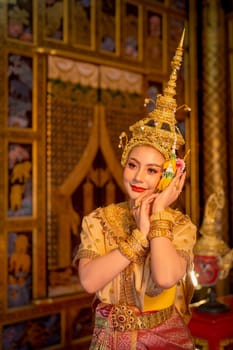 Beautiful Asian woman wear Thai ancient traditional dress action of dancing in front of Thai painting as background in public place.