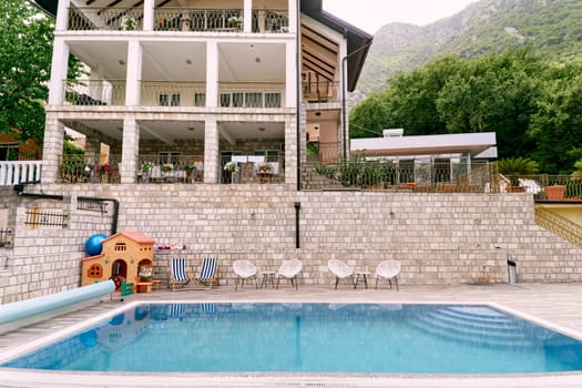 Wicker chairs with tables stand in front of the pool near a private hotel. High quality photo