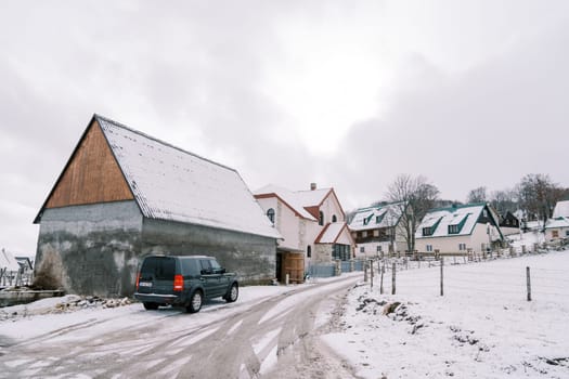 Black car stands near a house on the side of a snowy road. High quality photo