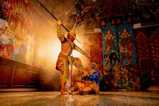 Khon or traditional Thai classic masked from the Ramakien monkey and giant characters action of fighting by spear together with Thai painting as background in public place.