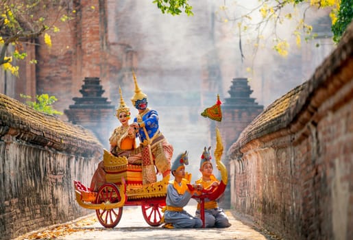 Khon or traditional Thai classic masked from the Ramakien characters woman and blue monkey stay together on traditional chariot in front of ancient building with mist or fog.