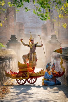 Vertical image of Asian man with old Thai traditional cloth hold weapon and stand and action of dance on traditional chariot also hold weapon stay in front of ancient building.