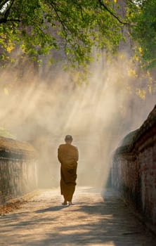 Vertical image of Back of Asian monk walk on the way along with old wall of ancient palace or building with linne beam light.