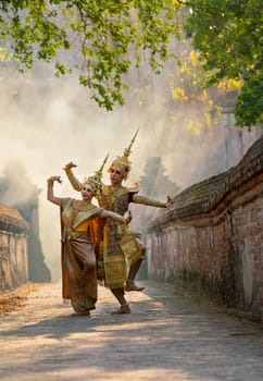 Vertical image of Asian man and woman wear Thai traditional dress and dance with beautifuul cultural style on the way with ancient wall and building in background.