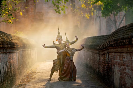 Asian man and woman wear Thai traditional dress and dance with beautifuul cultural style on the way with ancient wall and building in background.