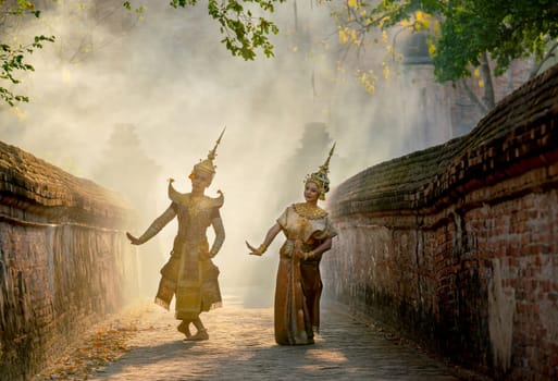 Asian man and woman wear Thai traditional dress and dance with beautifuul cultural style on the way with ancient wall and building in background.