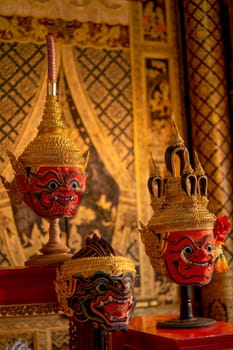 Vertical image of beautiful ancient traditional Thai pattern Pantomime or Khon masks are set up on wooden shelves with Thai painting as background of public place in Thailand.