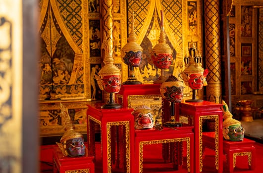 Side view of beautiful ancient traditional Thai pattern Pantomime or Khon masks are set up on wooden shelves with Thai painting as background of public place in Thailand.