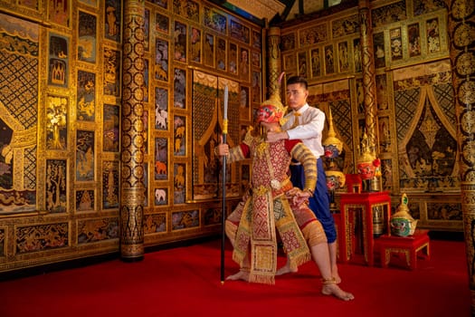 Asian man with Thai style cloth action of teaching to man wear ancient traditional Thai pattern Pantomime in room with Thai painting style on wall of public place.