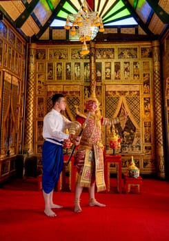 Asian man with Thai style cloth action of teaching to man wear ancient traditional Thai pattern Pantomime in room with Thai painting style on wall of public place.