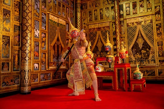 Khon or traditional Thai classic masked from the Ramakien monkey and red giant characters action of dance with spear in front of Thai painting as background in public place.