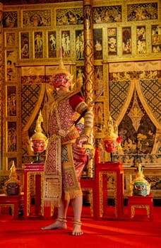 Vertical image of Khon or traditional Thai classic masked from the Ramakien with Red giant character stand with spear and look forward with Thai painting wall in background.