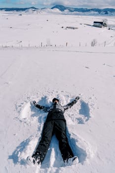 Young woman in a ski suit makes a snow angel in the snow. High quality photo