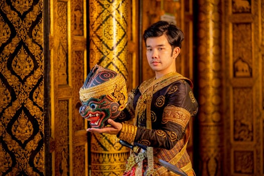 Asian man with traditional cloths relate to Khon or Thai classic masked stand with holding black monkey mask in front of windows of public building also look at camera.