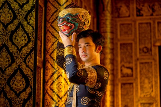 Asian man with traditional cloth relate to Khon or Thai classic masked with holding black monkey mask stand in front of windows of public building.