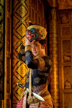 Vertical image of Asian man with traditional cloth relate to Khon or Thai classic masked with holding black monkey mask stand in front of windows of public building.