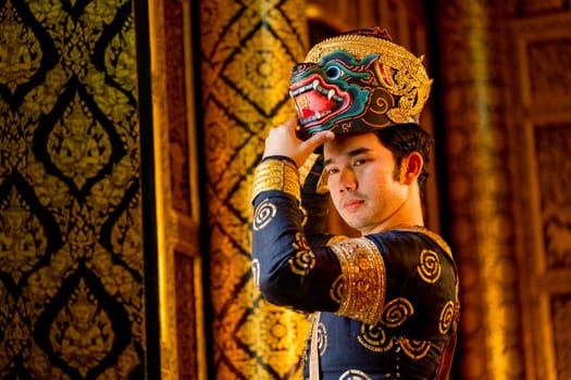 Close up Asian man with traditional cloth relate to Khon or Thai classic masked with holding black monkey mask stand in front of windows of public building.