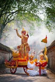 Vertical image of Khon or traditional Thai classic masked from the Ramakien as character of red giant stand and dance on traditional chariot also hold weapon stay in front of ancient building.