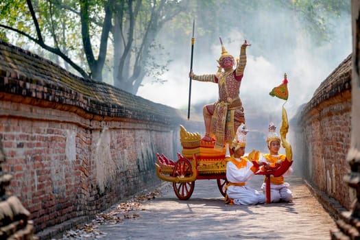 Khon or traditional Thai classic masked from the Ramakien as character of red giant stand and dance on traditional chariot also hold weapon stay in front of ancient building with mist or fog.