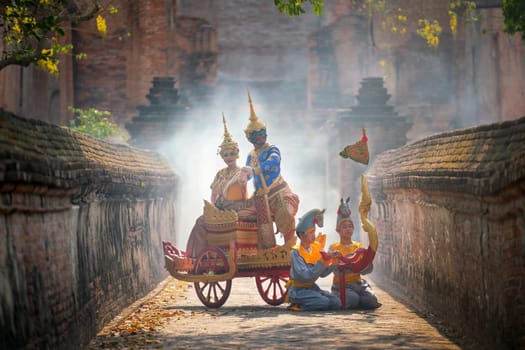 Khon Thai classic masked from the Ramakien with characters of woman and blue monkey stay together on traditional chariot in front of ancient building with mist or fog.