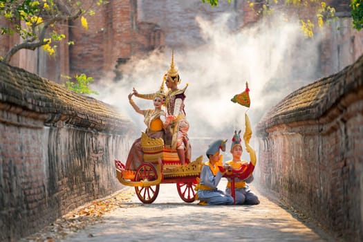 Asian man and woman with Thai old traditional dress stay together on traditional chariot in front of ancient building.