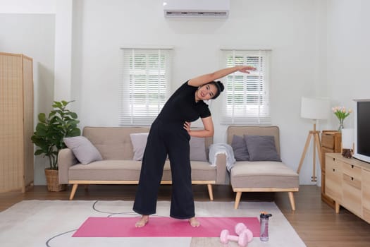 Fat woman exercising at home A beautiful oversized woman in a sports bra and casual pants stands in the living room and exercises..