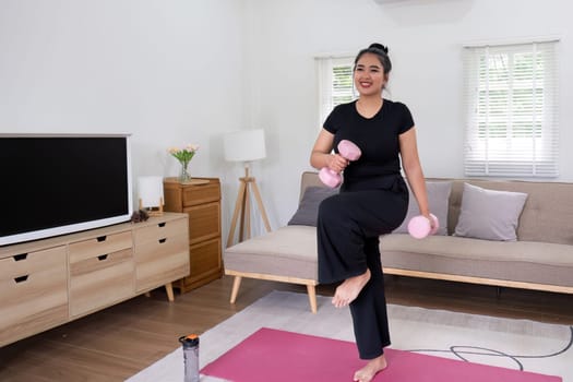 Fat woman exercising at home A beautiful oversized woman in a sports bra and casual pants stands in the living room and exercises..