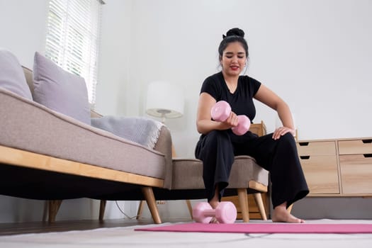 Fat woman exercising at home A beautiful oversized woman in a sports bra and casual pants sits in the living room and exercises