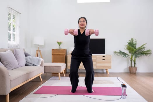 Fat woman exercising at home A beautiful oversized woman in a sports bra and casual pants stands in the living room and exercises..