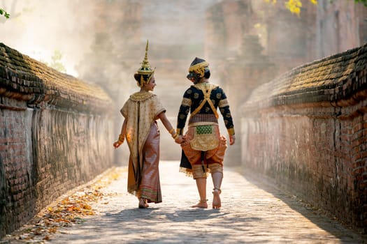 Beautiful Asian woman wear Thai traditional dress action of walking together with Thai classic masked from the Ramakien character as black monkey with ancient wall and buildin in backgground.