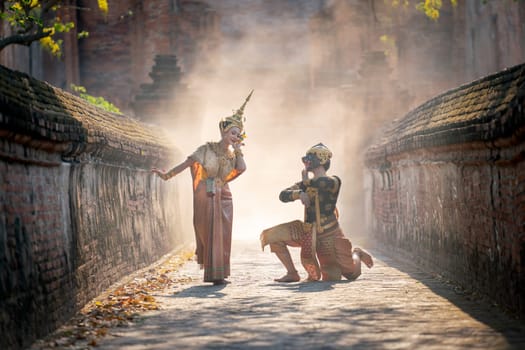 Beautiful Asian woman wear Thai traditional dress action of dancing together with Thai classic masked from the Ramakien character as black monkey with ancient wall and buildin in backgground.