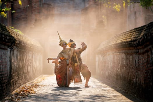 Beautiful Asian woman wear Thai traditional dress action of dancing together with Thai classic masked from the Ramakien character as black monkey with ancient wall and buildin in mist background.