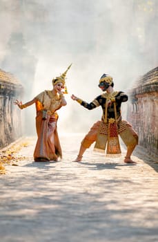 Vertical beautiful Asian woman wear Thai traditional dress action of dancing together with Thai classic masked from the Ramakien character as black monkey with ancient wall and buildin in background.