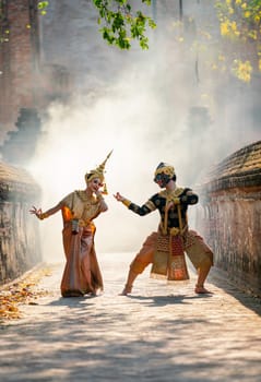 Beautiful Asian woman wear Thai traditional dress action of dancing together with Thai classic masked from the Ramakien character as black monkey with ancient wall and buildin in backgground.