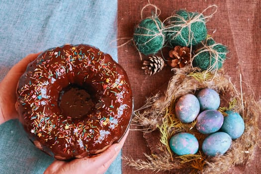 Woman holding chocolate cake with powder next to space galactic Easter eggs in nest next to bump and green filler