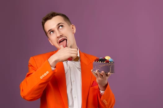 happy man in orange jacket eating cream cake on purple background