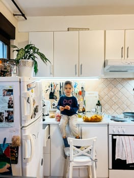 Little girl sits on the table in the kitchen near the refrigerator. High quality photo